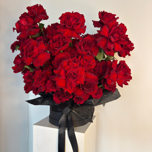 Bouquet of red flowers with a black ribbon on a white pedestal against a light background
