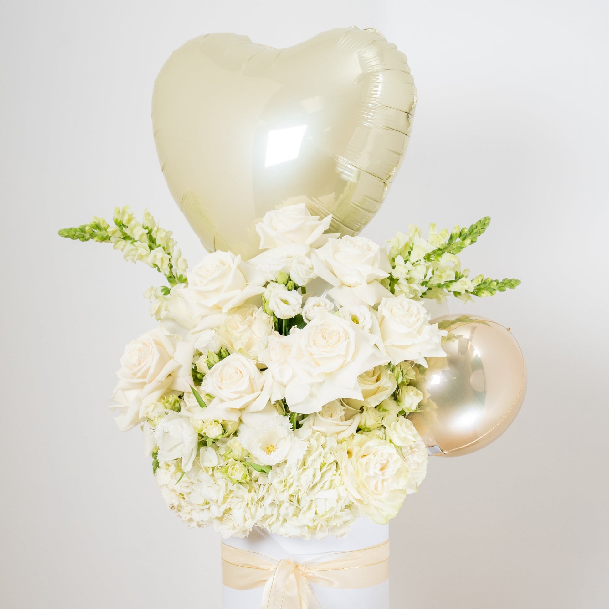 white flower arrangement with a heart balloon on topinside of a white box