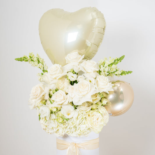 white flower arrangement with a heart balloon on topinside of a white box
