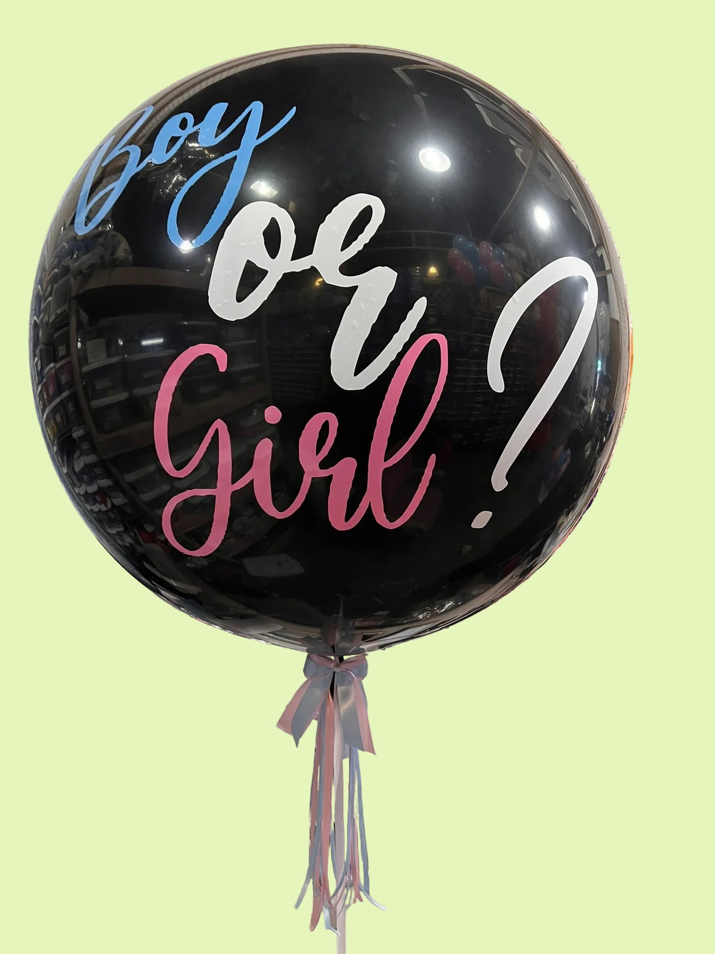 A large black balloon with the words 'Boy or Girl?' in blue, white, and pink script, tied to a table in a party decoration setup.