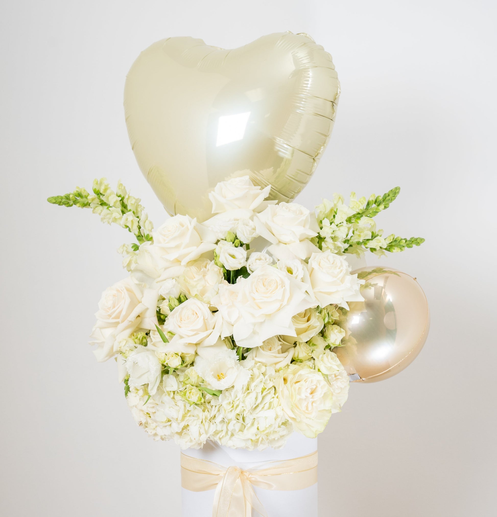 white flower arrangement with a heart balloon on topinside of a white box