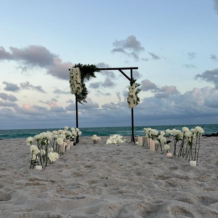 Beach wedding setup with floral arch and decorations on a sandy beach.