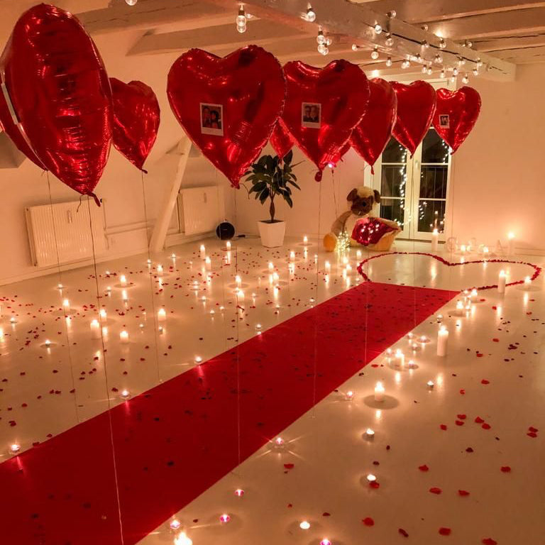Decorated room with heart-shaped balloons, candles, and red accents for a romantic setting.