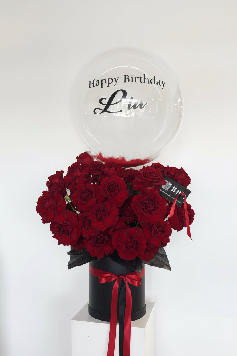 Bouquet of red flowers in a black vase with a personalized balloon on a white background